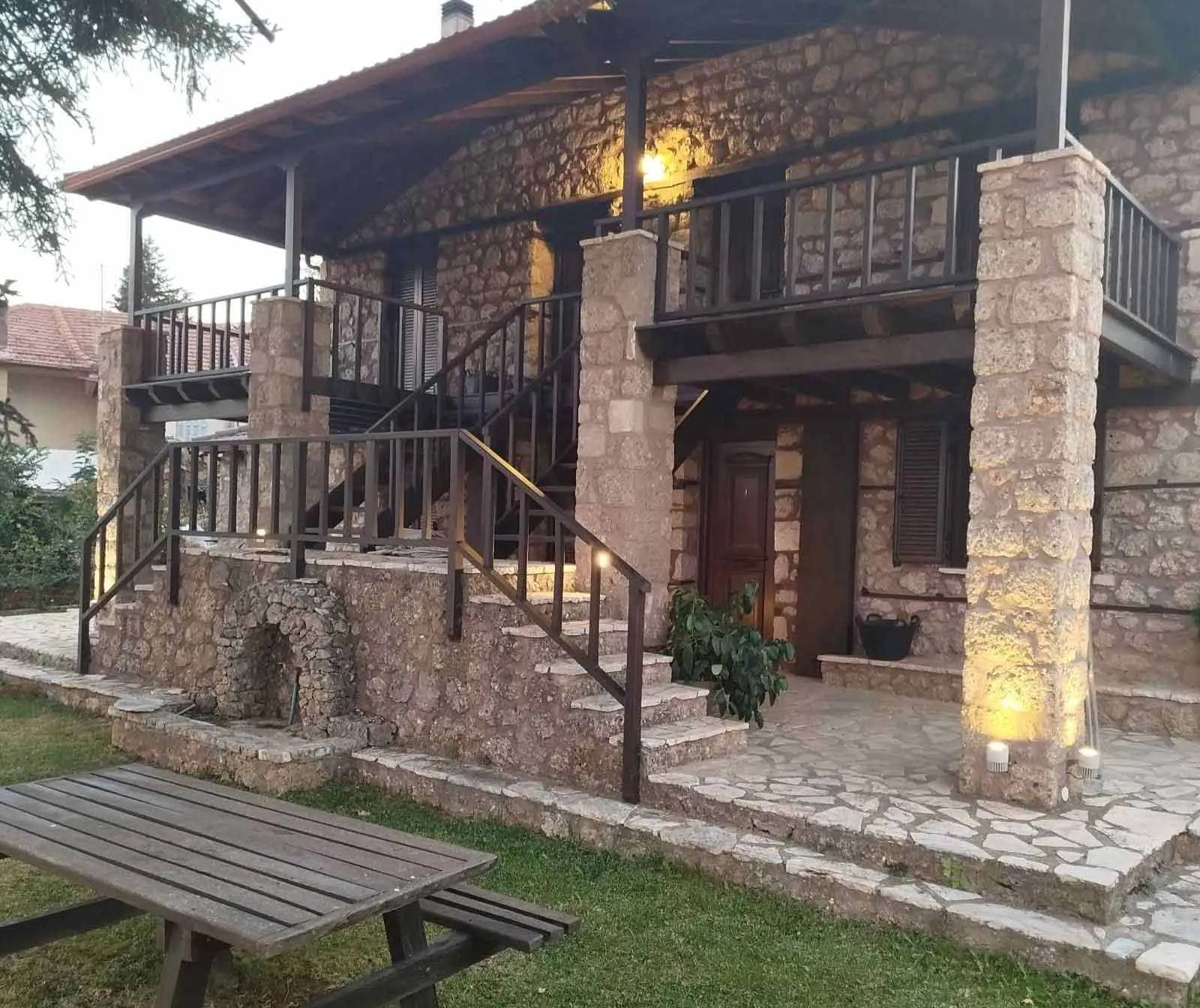 Η πέτρινη πρόσοψη με τα φωτισμένα μπαλκόνια και τη σκάλα, το σούρουπο